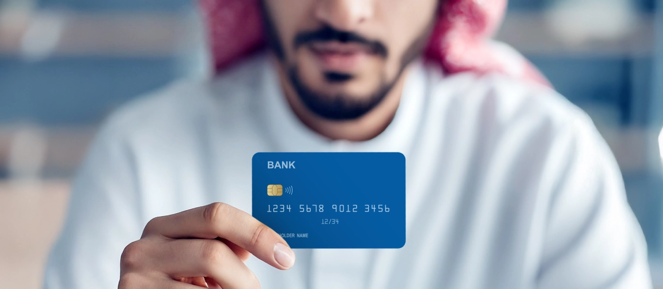 Man in Saudi attire holding a blue bank card, symbolizing digital payments or financial services.